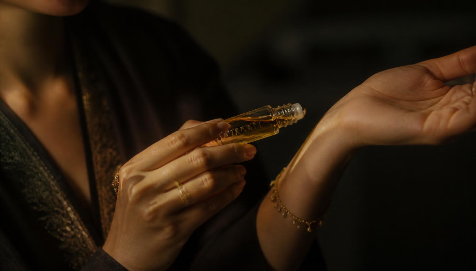 Close-up of a glass attar roll-on being applied to the inside of a wrist in warm low light